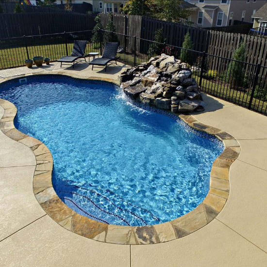 A backyard pool with a waterfall made with natural stones.